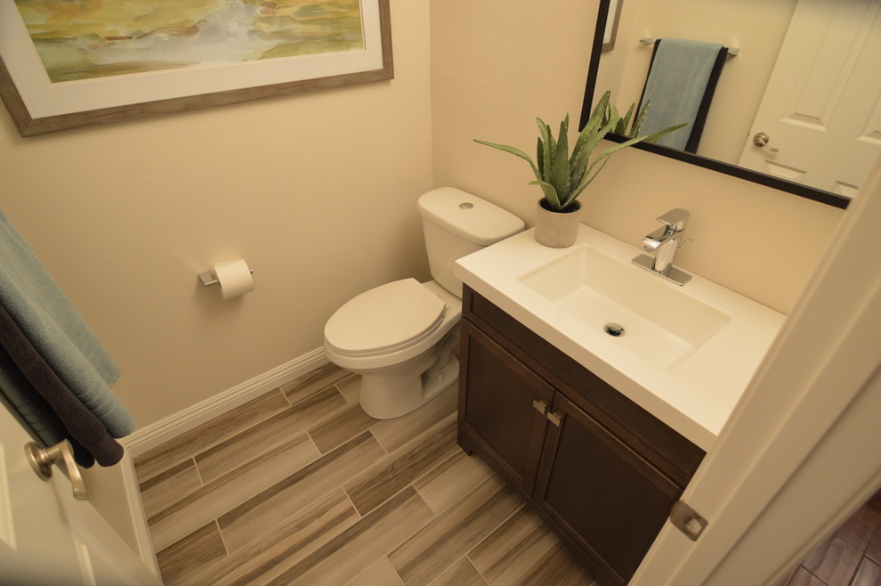 Photo of a mid-sized contemporary powder room in Los Angeles with shaker cabinets, dark wood cabinets, a two-piece toilet, vinyl floors, an integrated sink and solid surface benchtops.