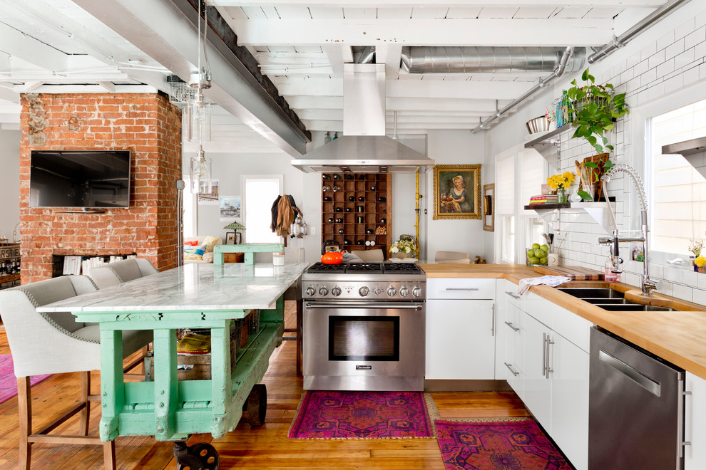 Design ideas for an eclectic l-shaped open plan kitchen in Providence with a triple-bowl sink, flat-panel cabinets, white cabinets, wood benchtops, white splashback, subway tile splashback, stainless steel appliances, medium hardwood floors and with island.