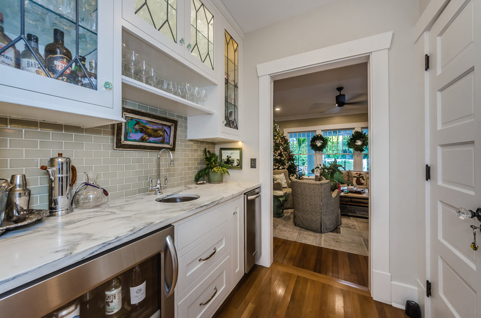 This is an example of a transitional single-wall wet bar in Tampa with an undermount sink, shaker cabinets, white cabinets, grey splashback, subway tile splashback, medium hardwood floors, brown floor and grey benchtop.