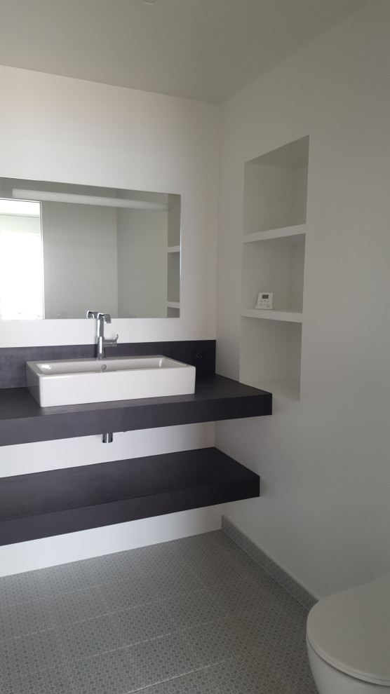 Photo of a small modern 3/4 bathroom in Nantes with a curbless shower, a wall-mount toilet, white walls, cement tiles, a drop-in sink, concrete benchtops, blue floor and black benchtops.