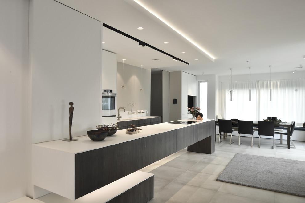 Inspiration for a large contemporary galley open plan kitchen in Hamburg with flat-panel cabinets, dark wood cabinets, solid surface benchtops, white appliances, grey floor, an integrated sink, concrete floors and a peninsula.