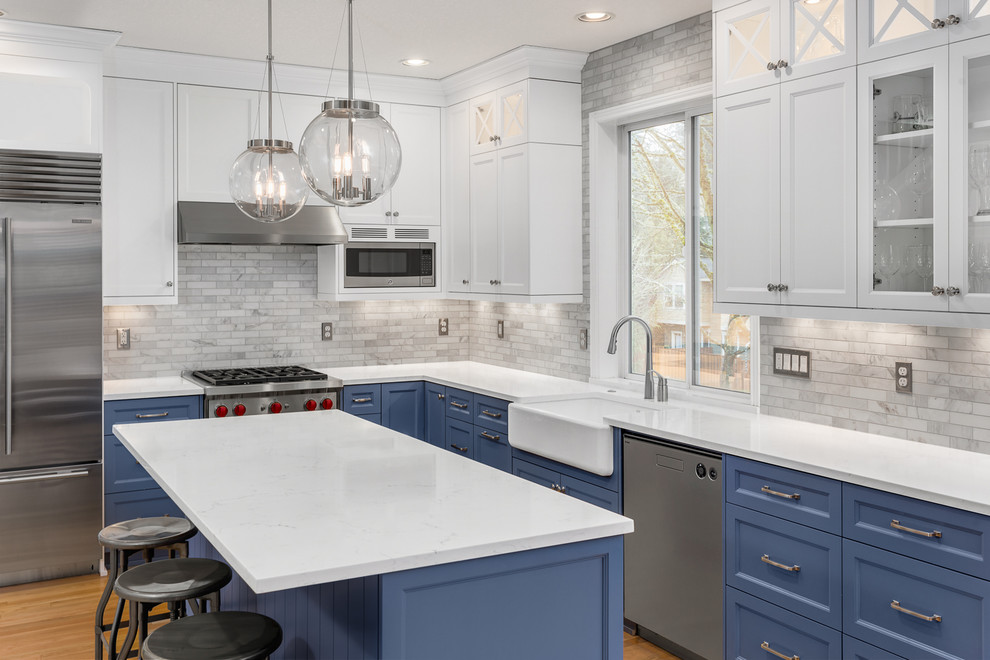 Inspiration for a mid-sized transitional l-shaped eat-in kitchen in Portland with a farmhouse sink, recessed-panel cabinets, blue cabinets, quartz benchtops, white splashback, marble splashback, stainless steel appliances, with island, medium hardwood floors and brown floor.