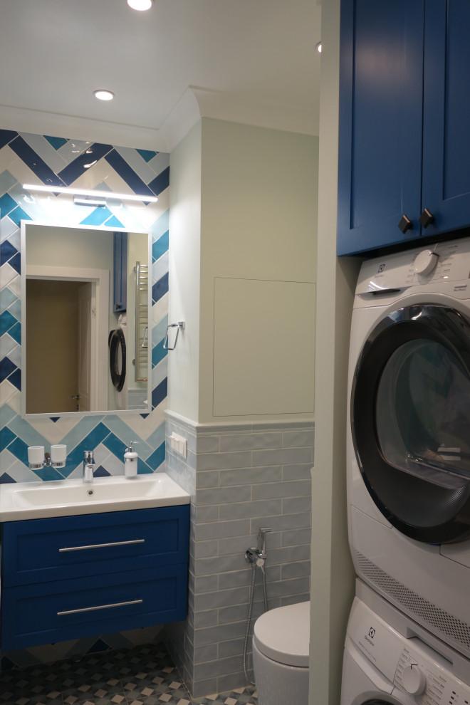 Пример оригинального дизайна: главная, серо-белая ванная комната среднего размера со стиральной машиной в морском стиле с фасадами с выступающей филенкой, синими фасадами, полновстраиваемой ванной, инсталляцией, синей плиткой, керамической плиткой, синими стенами, полом из керамогранита, накладной раковиной, столешницей из искусственного камня, синим полом, белой столешницей, тумбой под одну раковину, подвесной тумбой и многоуровневым потолком