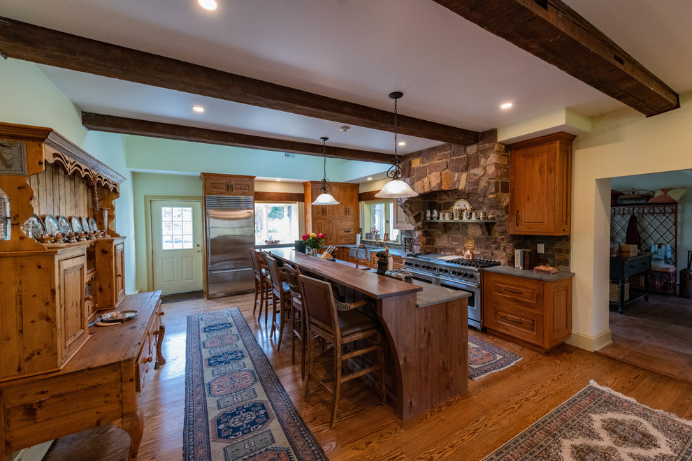 Eat-in kitchen - large rustic l-shaped medium tone wood floor and brown floor eat-in kitchen idea in Philadelphia with a farmhouse sink, raised-panel cabinets, distressed cabinets, soapstone countertops, multicolored backsplash, stone tile backsplash, stainless steel appliances, an island and blue countertops