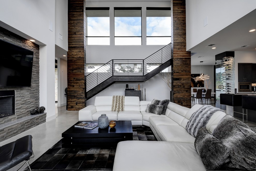 This is an example of a large contemporary open concept family room in Austin with white walls, concrete floors, a wall-mounted tv and grey floor.
