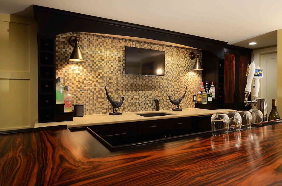 Inspiration for a mid-sized transitional galley seated home bar in New York with an undermount sink, flat-panel cabinets, black cabinets, limestone benchtops, beige splashback, stone tile splashback, dark hardwood floors and brown floor.