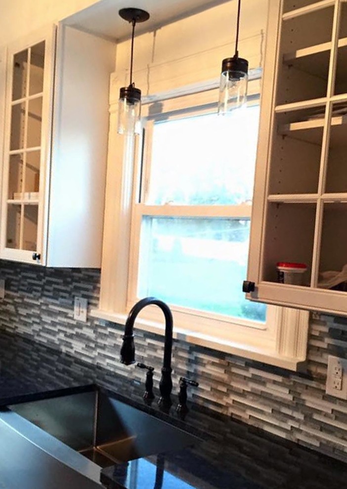 Kitchen pantry - mid-sized transitional l-shaped medium tone wood floor and brown floor kitchen pantry idea with a farmhouse sink, recessed-panel cabinets, white cabinets, granite countertops, multicolored backsplash, glass tile backsplash, stainless steel appliances, no island and black countertops
