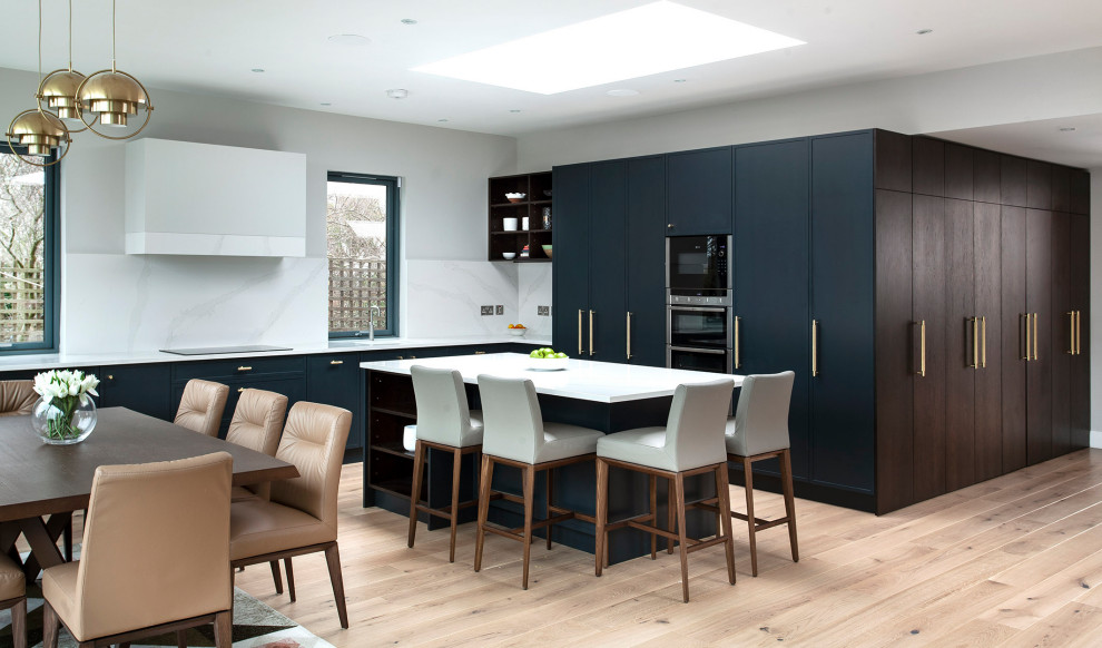 This is an example of a large contemporary l-shaped eat-in kitchen in Dublin with an undermount sink, flat-panel cabinets, dark wood cabinets, quartzite benchtops, white splashback, black appliances, light hardwood floors, with island and white benchtop.