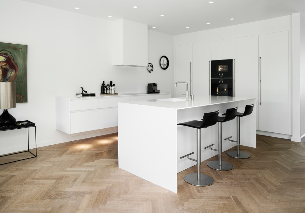Inspiration for a scandinavian open plan kitchen in Odense with flat-panel cabinets, white cabinets, black appliances, with island, white benchtop, an integrated sink, light hardwood floors and beige floor.