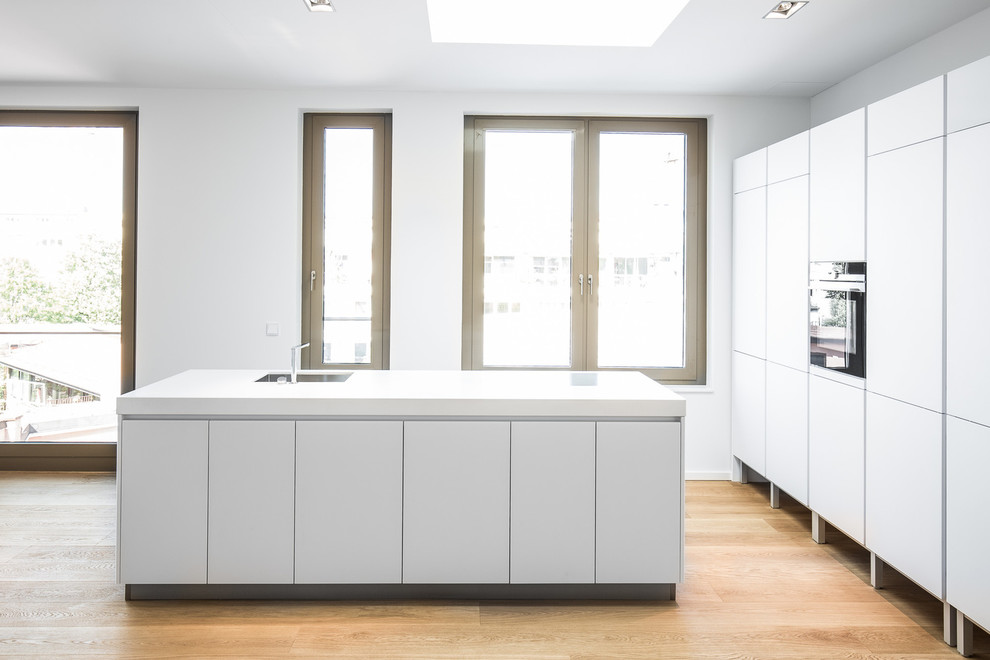 Photo of a mid-sized contemporary open plan kitchen in Munich with an undermount sink, flat-panel cabinets, white cabinets, panelled appliances, medium hardwood floors and with island.