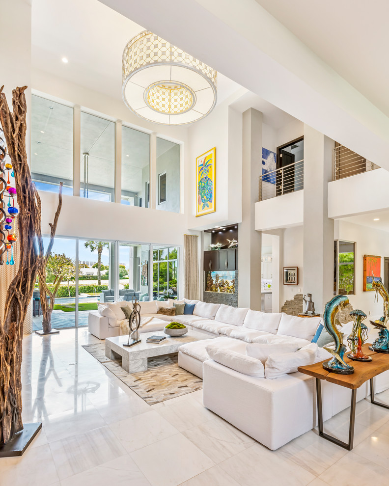 This is an example of a large tropical open concept living room in Miami with white walls, white floor, marble floors, a standard fireplace and a metal fireplace surround.