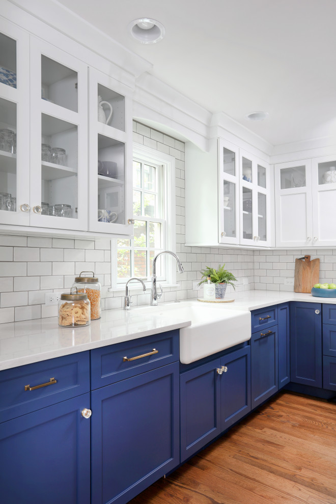 Transitional medium tone wood floor and brown floor eat-in kitchen photo in Chicago with a farmhouse sink, beaded inset cabinets, blue cabinets, quartz countertops, white backsplash, glass tile backsplash and white countertops
