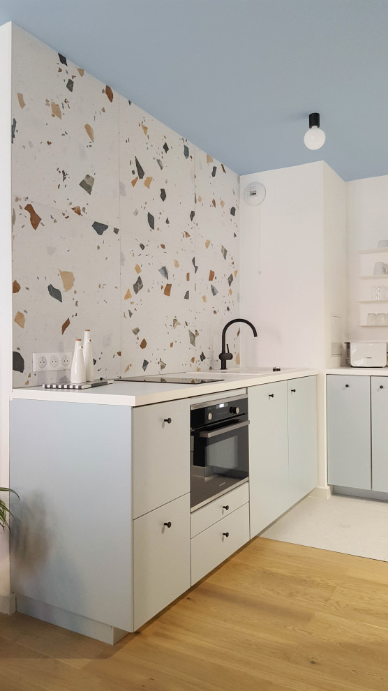 This is an example of a mid-sized eclectic u-shaped open plan kitchen with an undermount sink, blue cabinets, laminate benchtops, multi-coloured splashback, glass tile splashback, terrazzo floors, white floor and white benchtop.