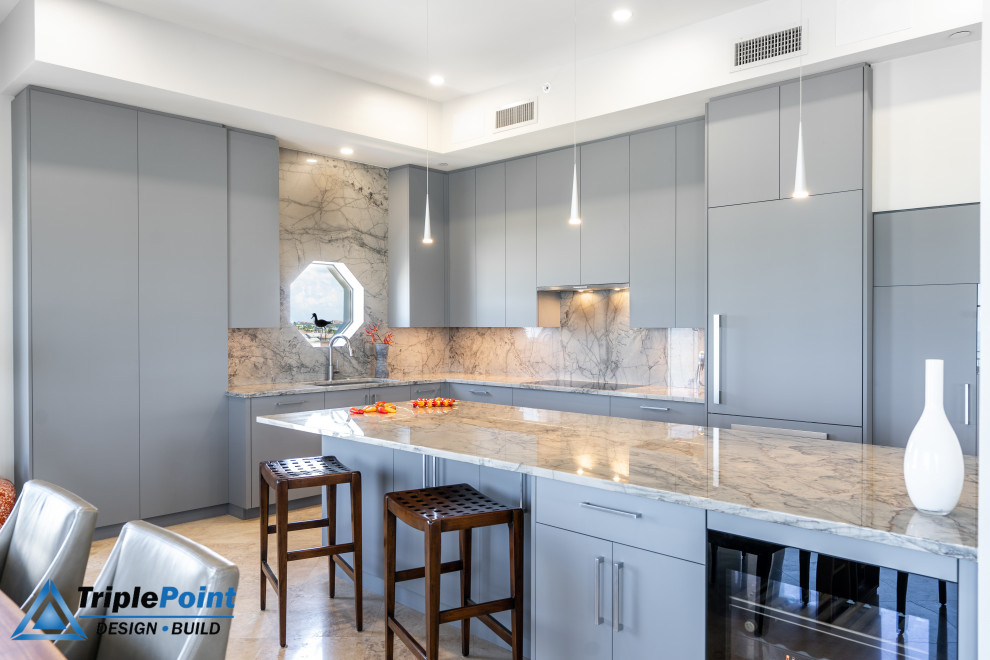 Large contemporary l-shaped open plan kitchen in Tampa with an undermount sink, flat-panel cabinets, grey cabinets, granite benchtops, grey splashback, granite splashback, stainless steel appliances, porcelain floors, with island, beige floor, grey benchtop, recessed and vaulted.