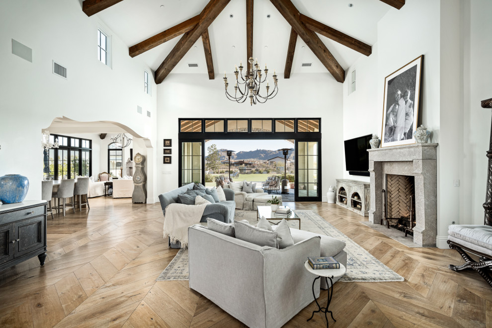 This is an example of an open concept living room in Phoenix with white walls, medium hardwood floors, a standard fireplace, a wall-mounted tv, brown floor, exposed beam and vaulted.