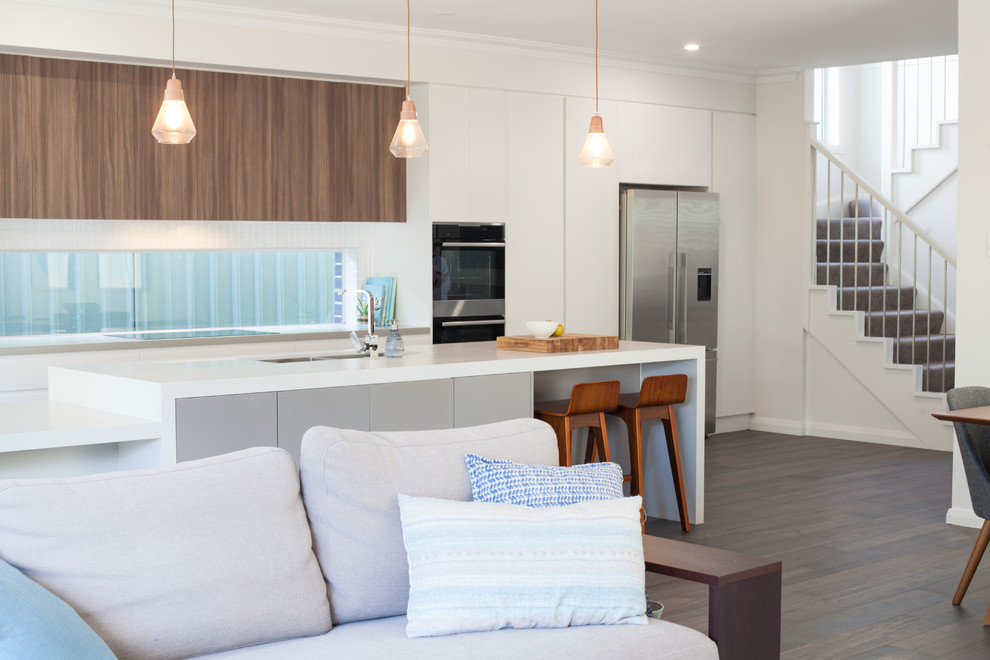 Large contemporary galley open plan kitchen in Sydney with an undermount sink, white cabinets, quartz benchtops, window splashback, stainless steel appliances, porcelain floors, with island and brown floor.