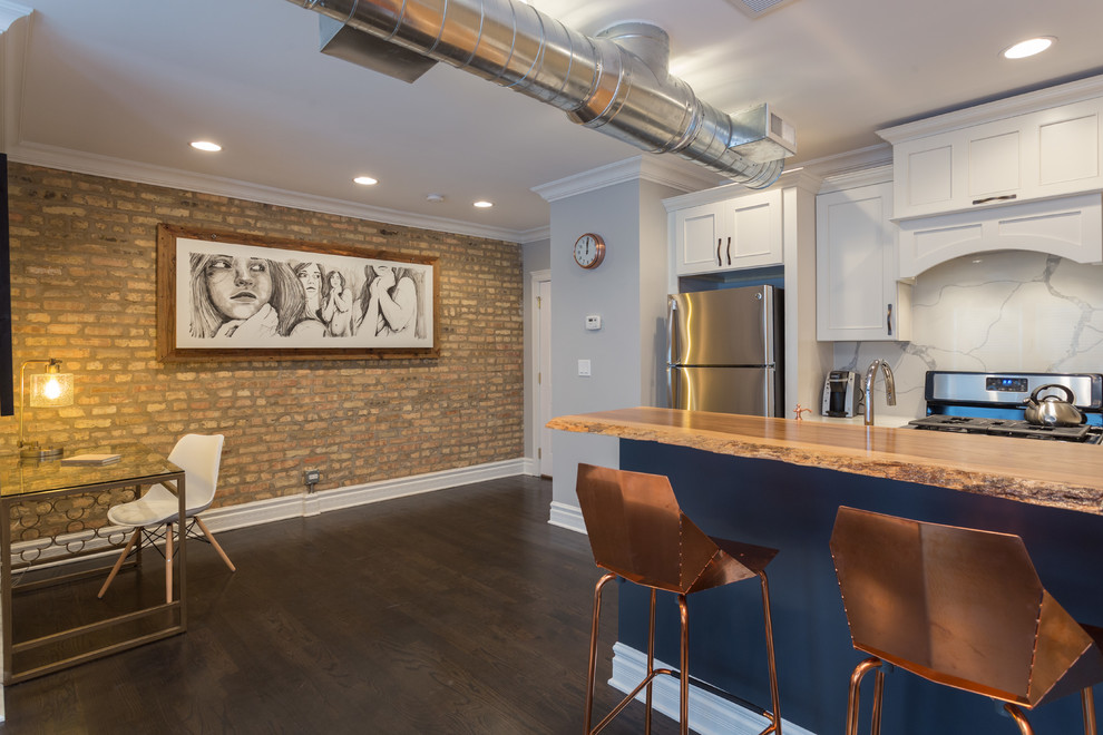 This is an example of a mid-sized industrial galley open plan kitchen in Chicago with an undermount sink, flat-panel cabinets, white cabinets, wood benchtops, white splashback, marble splashback, stainless steel appliances, dark hardwood floors, with island and brown floor.