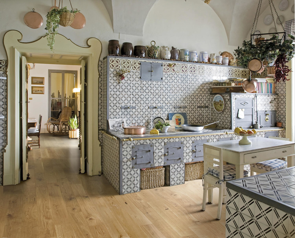 Country eat-in kitchen in Naples with tile benchtops, multi-coloured splashback, ceramic splashback and light hardwood floors.