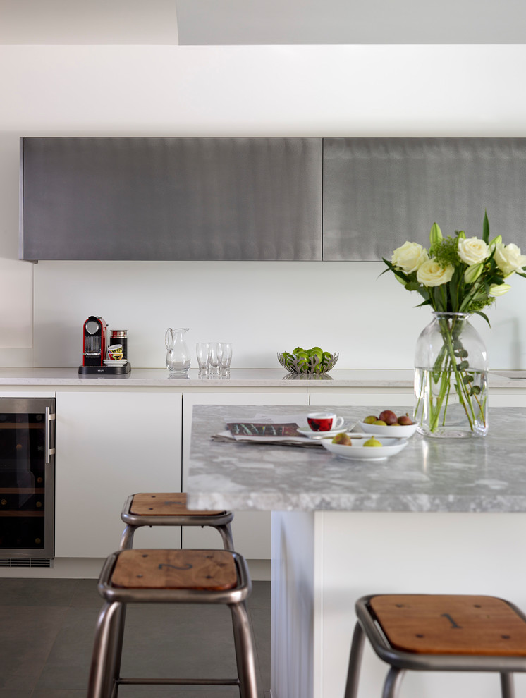 Large contemporary single-wall open plan kitchen in London with flat-panel cabinets, white cabinets, granite benchtops, white splashback, glass sheet splashback, with island, grey floor and grey benchtop.
