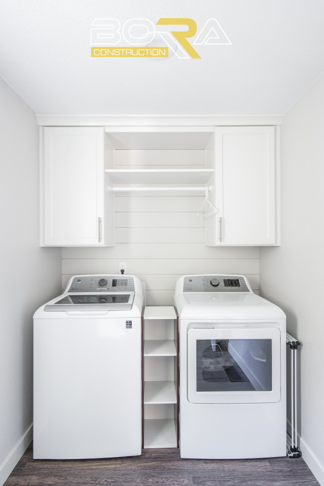 Inspiration for a mid-sized single-wall utility room in Seattle with an undermount sink, shaker cabinets, white cabinets, white walls, medium hardwood floors, a side-by-side washer and dryer and brown floor.