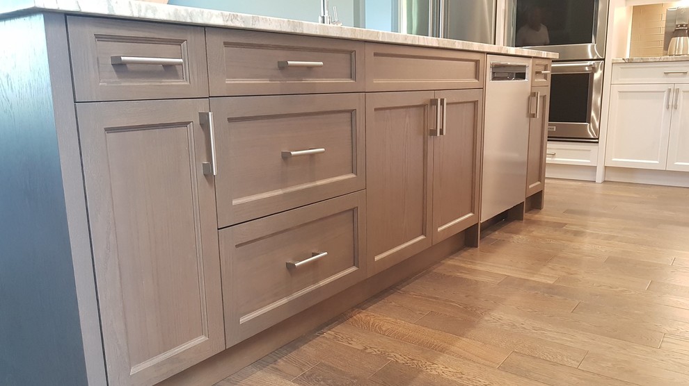 Photo of a large transitional l-shaped eat-in kitchen in Vancouver with shaker cabinets, granite benchtops, an undermount sink, grey splashback, stainless steel appliances, with island, brown floor, brown benchtop, white cabinets, ceramic splashback and medium hardwood floors.