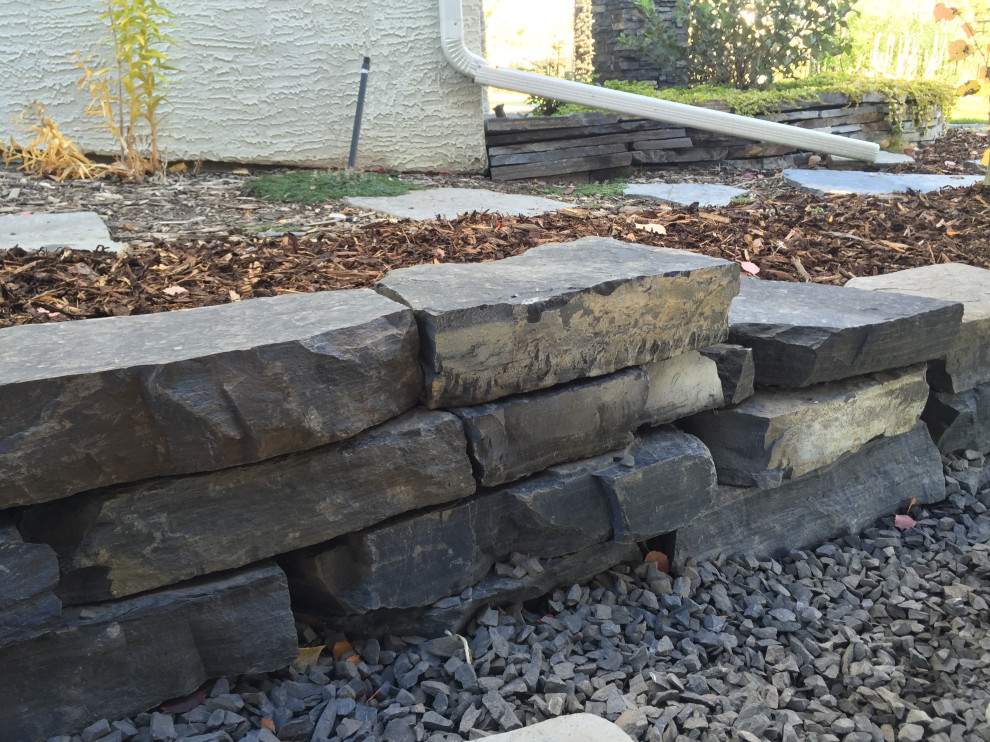 Photo of a mid-sized sloped garden in Calgary with a retaining wall and natural stone pavers.