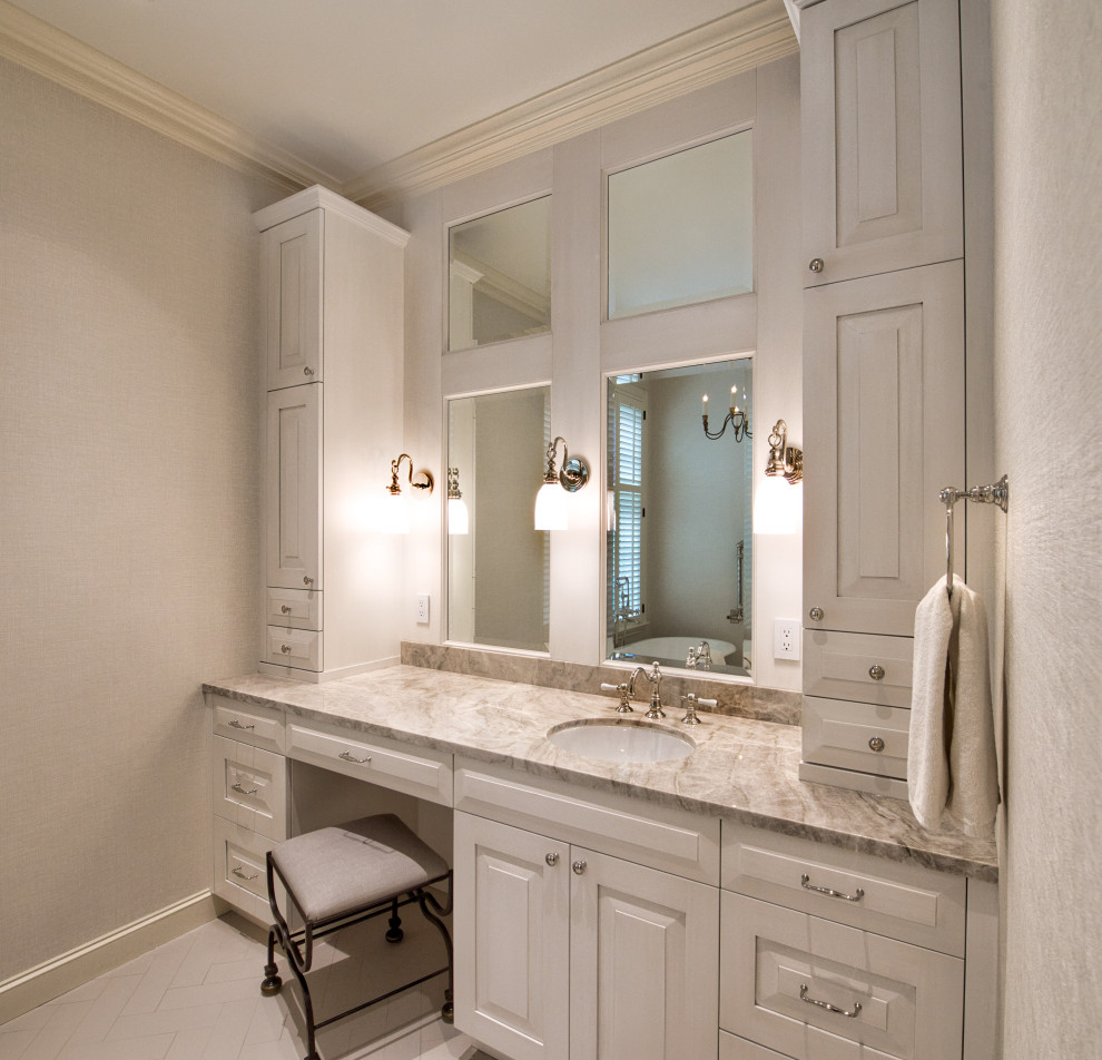 This is an example of a traditional master bathroom in Houston with raised-panel cabinets, beige cabinets, a freestanding tub, beige walls, porcelain floors, an undermount sink, quartzite benchtops, beige floor, beige benchtops, a laundry, a built-in vanity and wallpaper.