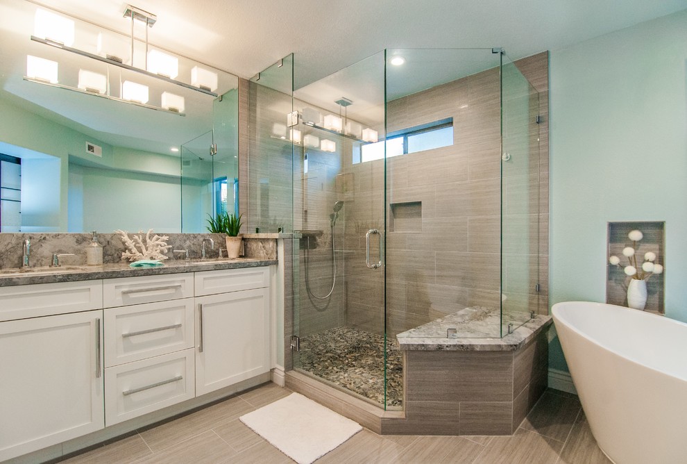 Photo of a large modern master bathroom in San Diego with shaker cabinets, white cabinets, a freestanding tub, a corner shower, gray tile, blue walls and an undermount sink.