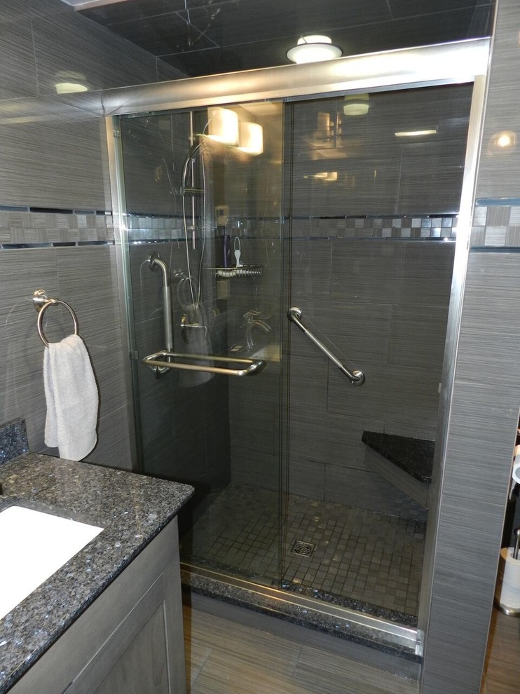 Example of a mid-sized transitional 3/4 gray tile and porcelain tile porcelain tile and gray floor alcove shower design with raised-panel cabinets, gray cabinets, white walls, an undermount sink, granite countertops and black countertops