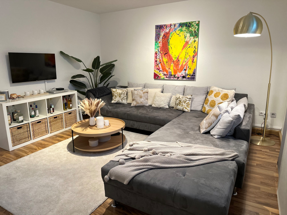 Photo of a mid-sized contemporary enclosed living room in Cologne with beige walls, laminate floors, a freestanding tv, brown floor and wallpaper.
