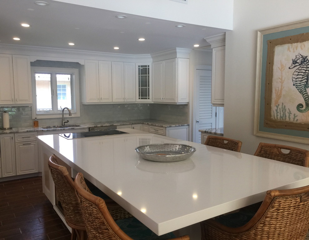 Example of a large beach style porcelain tile eat-in kitchen design with an undermount sink, raised-panel cabinets, white cabinets, quartzite countertops, blue backsplash, glass tile backsplash, stainless steel appliances and an island