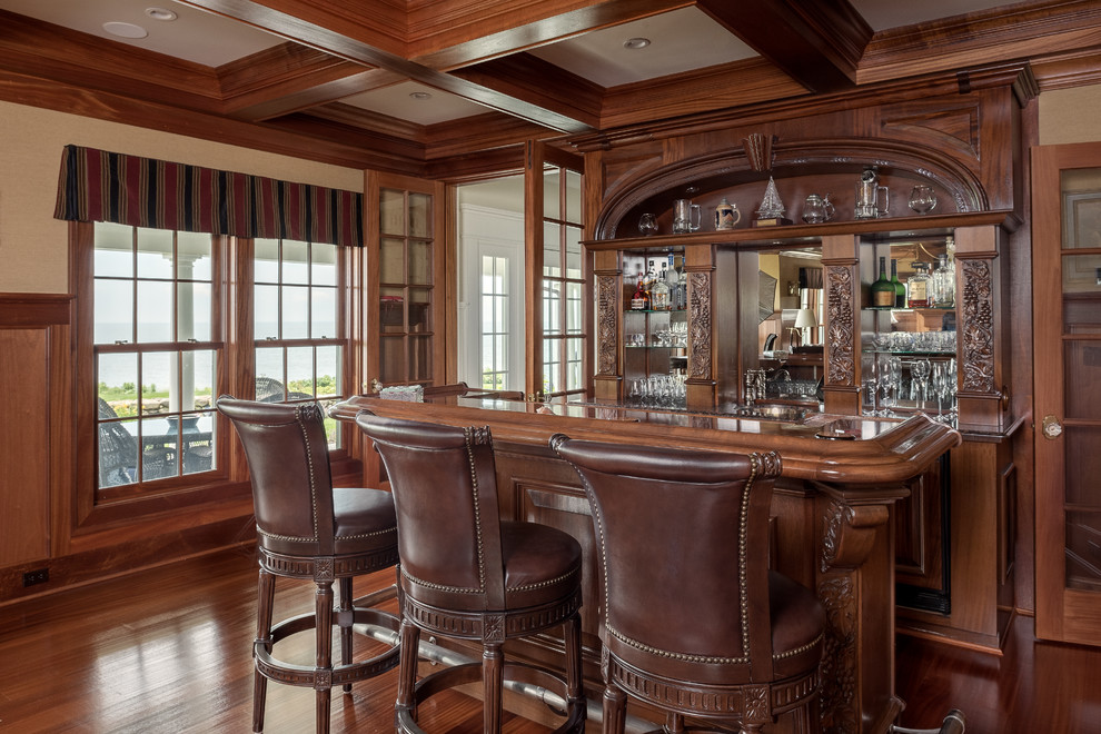 Large beach style seated home bar in Bridgeport with dark wood cabinets, marble benchtops, mirror splashback, medium hardwood floors and brown benchtop.