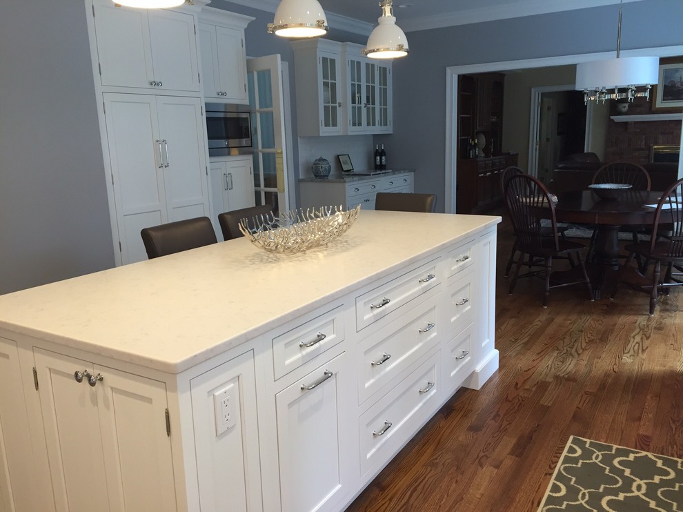 Example of a mid-sized transitional l-shaped medium tone wood floor eat-in kitchen design in Bridgeport with an undermount sink, shaker cabinets, white cabinets, solid surface countertops, white backsplash, subway tile backsplash, stainless steel appliances and an island