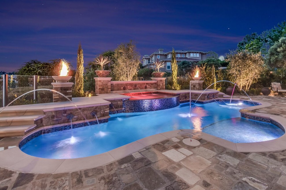 Inspiration for a large contemporary backyard custom-shaped pool in Orange County with a hot tub and natural stone pavers.