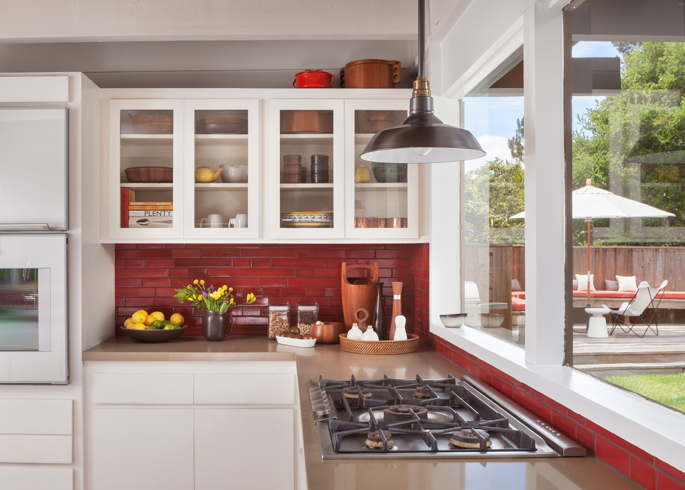 This is an example of a mid-sized midcentury galley open plan kitchen in San Francisco with an undermount sink, glass-front cabinets, white cabinets, soapstone benchtops, red splashback, ceramic splashback, stainless steel appliances, dark hardwood floors and a peninsula.