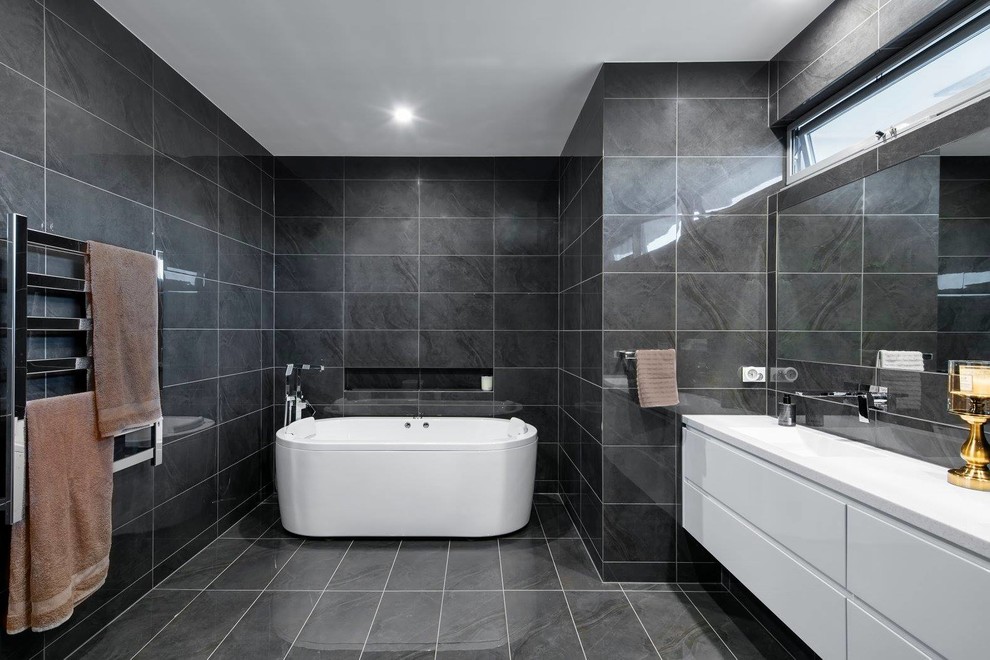 Photo of a large contemporary master bathroom in Adelaide with a freestanding tub, gray tile, porcelain tile, grey walls, porcelain floors, a drop-in sink, engineered quartz benchtops, flat-panel cabinets, white cabinets, an open shower, grey floor, an open shower and white benchtops.
