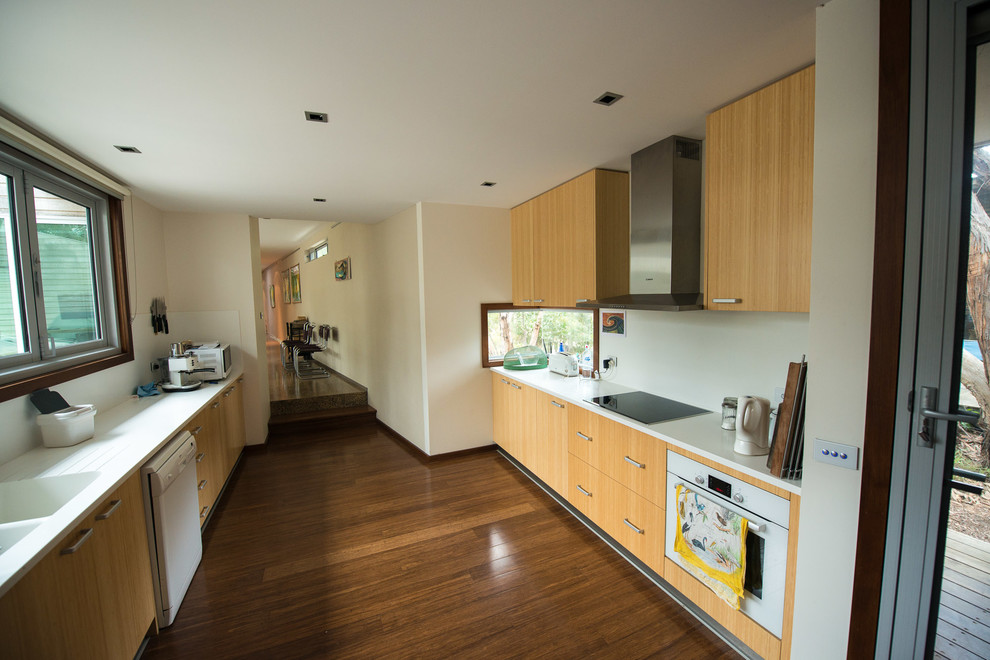 Inspiration for a large contemporary galley kitchen pantry in Melbourne with an integrated sink, flat-panel cabinets, light wood cabinets, solid surface benchtops, white splashback, glass sheet splashback, stainless steel appliances, bamboo floors and no island.