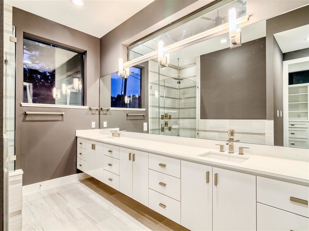 This is an example of a mid-sized modern master bathroom in Houston with an undermount sink, flat-panel cabinets, white cabinets, engineered quartz benchtops, a freestanding tub, a corner shower, a one-piece toilet, gray tile, porcelain tile, grey walls and porcelain floors.