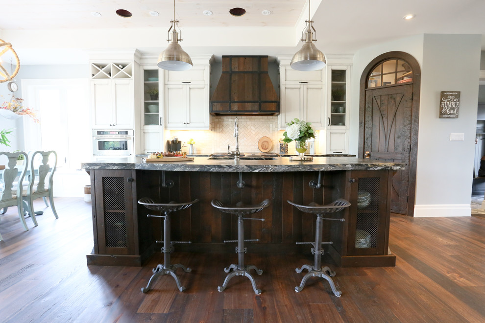 Inspiration for a large rustic l-shaped dark wood floor and brown floor open concept kitchen remodel in Toronto with an undermount sink, recessed-panel cabinets, white cabinets, beige backsplash, glass tile backsplash, stainless steel appliances, an island, onyx countertops and black countertops