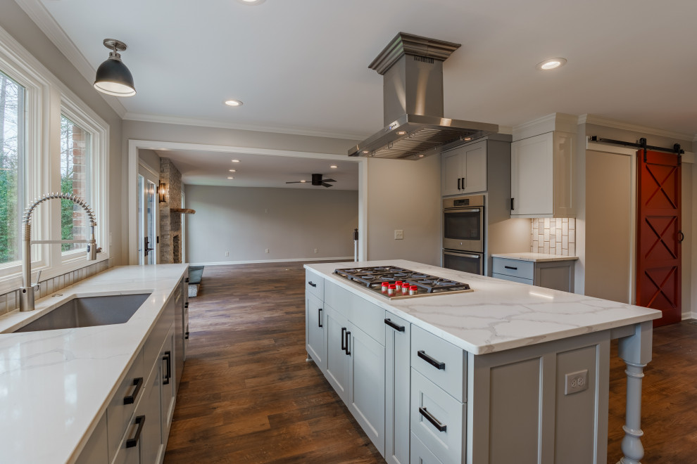 Example of a mid-sized transitional l-shaped vinyl floor and brown floor open concept kitchen design with an undermount sink, shaker cabinets, gray cabinets, quartz countertops, gray backsplash, marble backsplash, stainless steel appliances, an island and white countertops