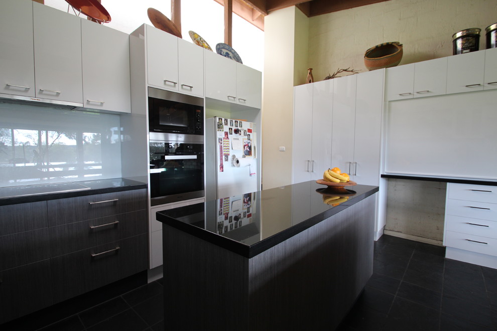 Photo of a large contemporary u-shaped open plan kitchen in Melbourne with a drop-in sink, flat-panel cabinets, grey cabinets, granite benchtops, white splashback, glass sheet splashback, stainless steel appliances, slate floors and multiple islands.