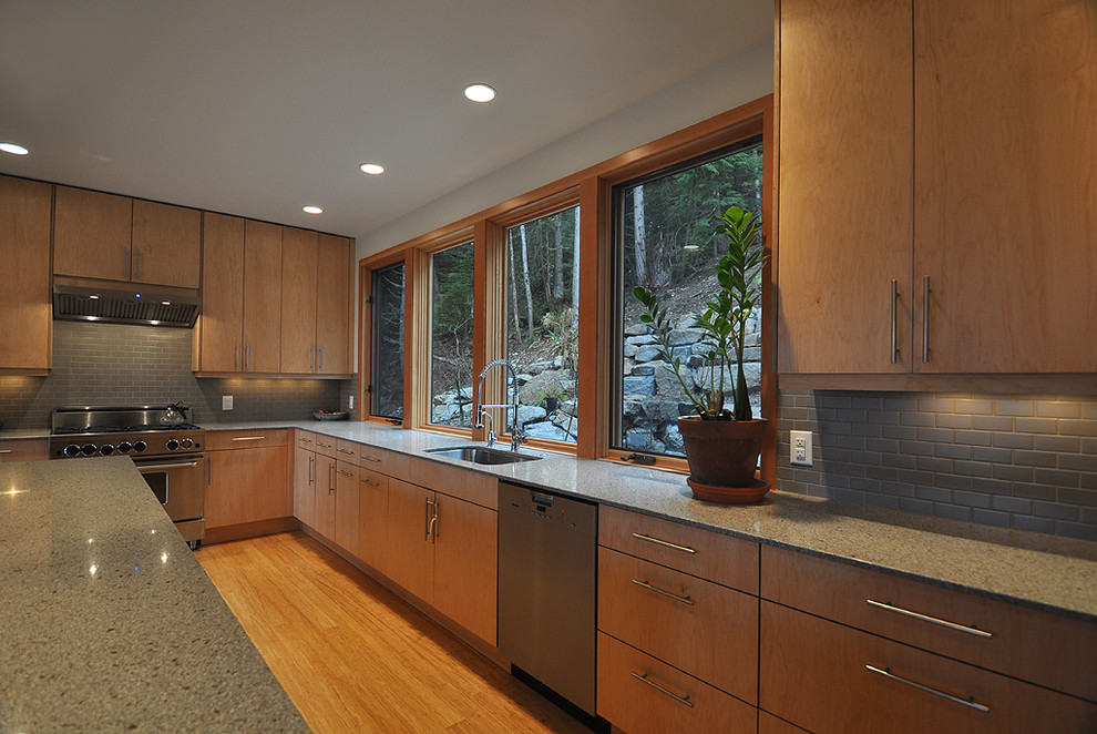This is an example of a large contemporary l-shaped open plan kitchen in Vancouver with an undermount sink, flat-panel cabinets, light wood cabinets, quartz benchtops, grey splashback, subway tile splashback, stainless steel appliances, bamboo floors and with island.