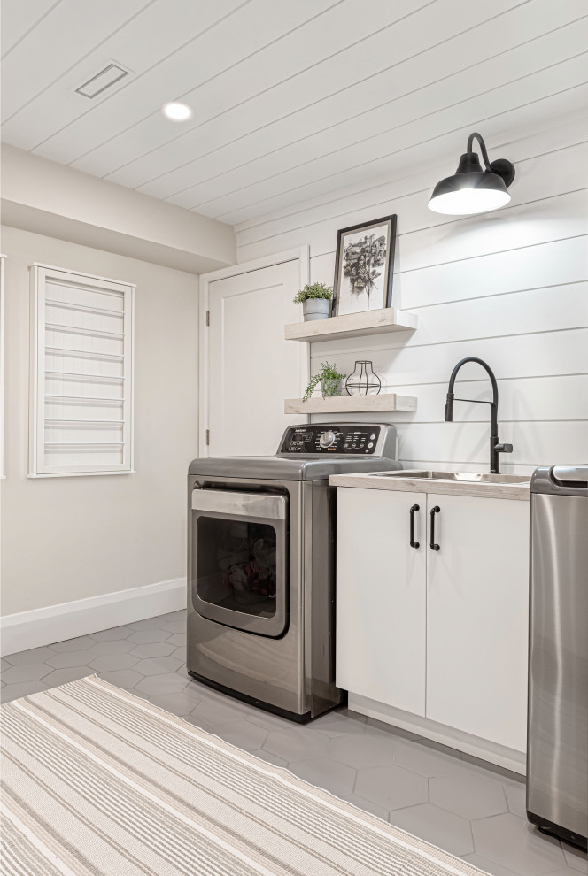 Mid-sized country dedicated laundry room in Toronto with a drop-in sink, flat-panel cabinets, white cabinets, laminate benchtops, grey walls, porcelain floors, a side-by-side washer and dryer, grey floor and timber.