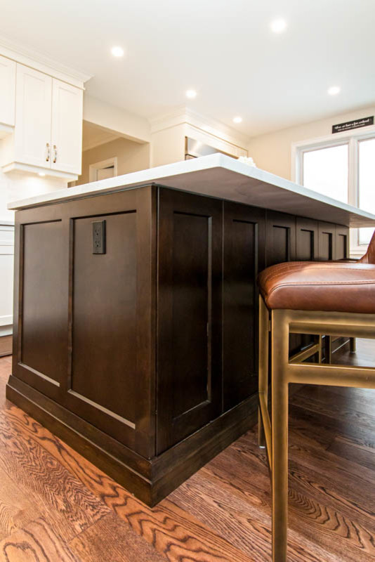 Open concept kitchen - mid-sized transitional l-shaped medium tone wood floor and brown floor open concept kitchen idea with an undermount sink, shaker cabinets, white cabinets, quartzite countertops, white backsplash, stone tile backsplash, stainless steel appliances, an island and white countertops