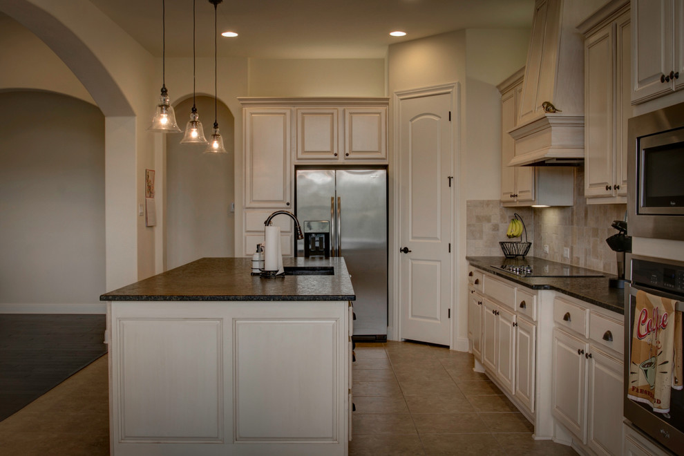 Inspiration for a rustic porcelain tile and beige floor kitchen pantry remodel in Austin with an undermount sink, raised-panel cabinets, white cabinets, granite countertops, beige backsplash, travertine backsplash, stainless steel appliances, an island and black countertops