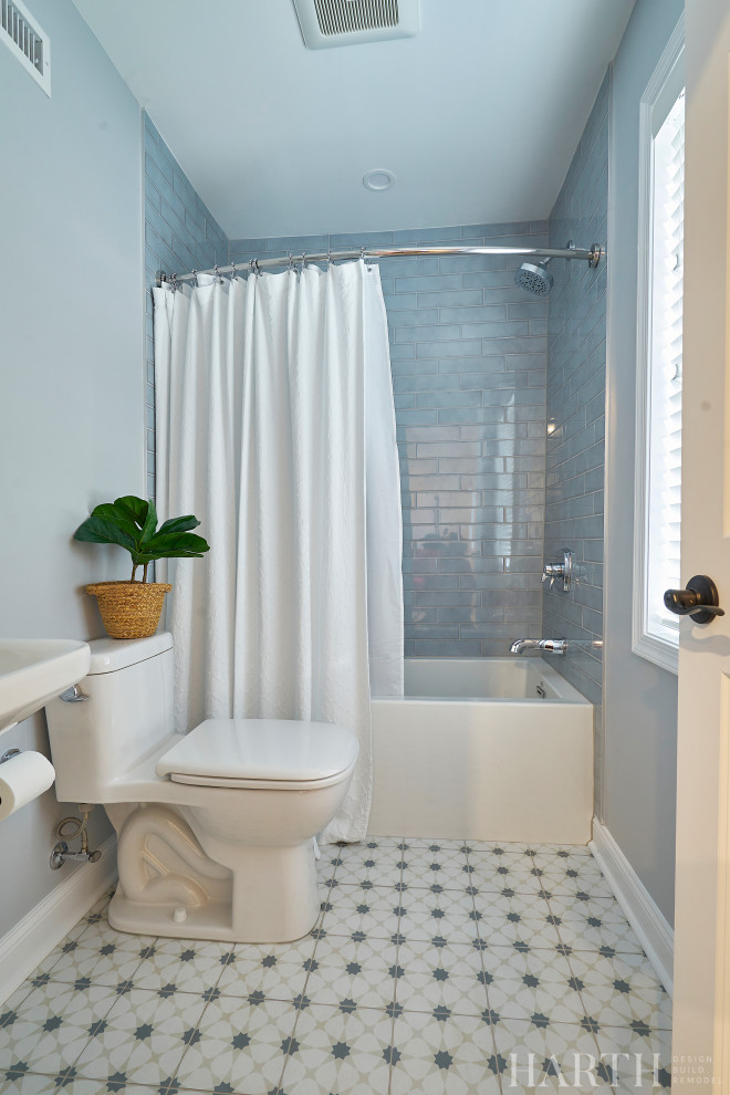 Inspiration for a mid-sized transitional 3/4 bathroom in Philadelphia with an alcove tub, a shower/bathtub combo, a two-piece toilet, blue tile, subway tile, blue walls, cement tiles, a pedestal sink, multi-coloured floor, a shower curtain, a niche, a single vanity and a freestanding vanity.