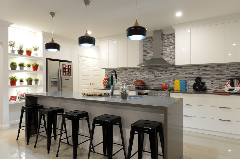 Photo of a mid-sized l-shaped kitchen in Other with a drop-in sink, flat-panel cabinets, white cabinets, multi-coloured splashback, mosaic tile splashback, stainless steel appliances, ceramic floors, beige floor, with island and grey benchtop.