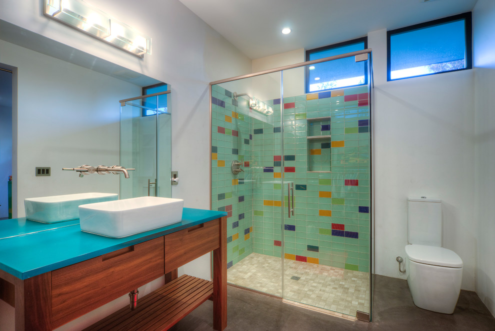 Photo of a mid-sized contemporary master bathroom in Phoenix with a vessel sink, medium wood cabinets, a corner shower, a two-piece toilet, glass tile, white walls, concrete floors, multi-coloured tile, blue benchtops and flat-panel cabinets.