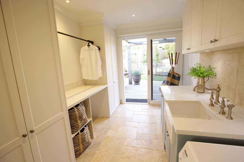 Photo of a contemporary laundry room in Melbourne with a farmhouse sink, shaker cabinets, blue cabinets, quartz benchtops, beige walls and travertine floors.