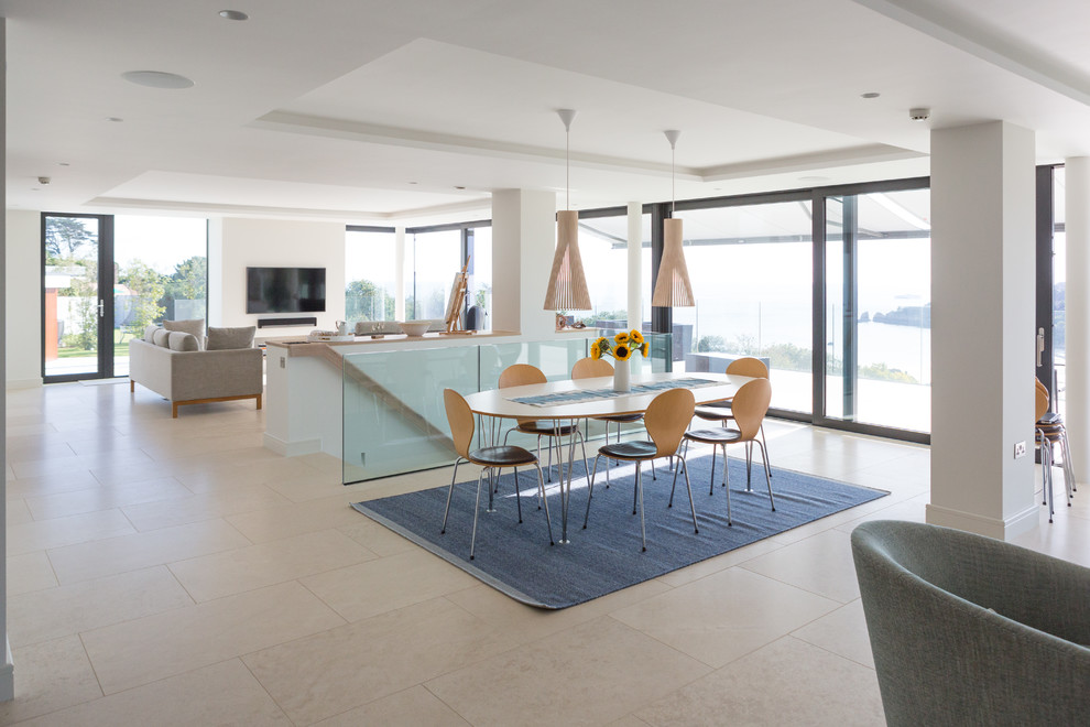 This is an example of a contemporary open plan dining in Channel Islands with white walls, no fireplace and beige floor.